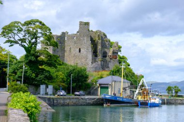 Kral Johns Kalesi 'nin heybetli kalıntıları limanda demirlemiş mavi bir balıkçı teknesinin arkasında duruyor. Ortaçağ tarihiyle modern deniz yaşamını harmanlıyor..