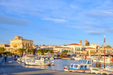 Aegina, Yunanistan - 31 Ocak 2026: Geleneksel balıkçı tekneleri, adanın ikonik 19. yüzyıl mimarisi ve öğleden sonra güneşinin yumuşak parıltısı tarafından çerçevelenen Aegina limanının sakin sularında sallanıyor.