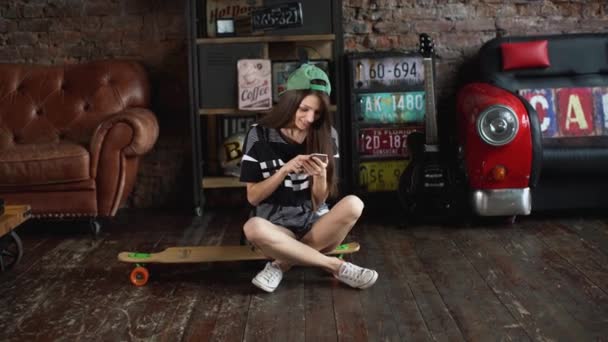 Girl sitting on skateboard with phone — Stock Video