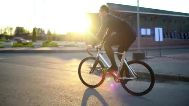 Чоловік їде на фіксованому велосипеді на дорозі на заході сонця — стокове відео