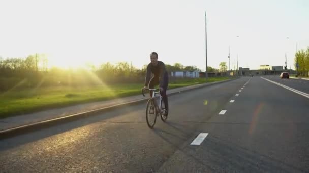 Hombre montando bicicleta de engranajes fijos en la carretera al atardecer — Vídeo de stock