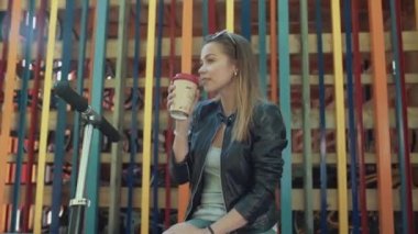 Güzel genç mutlu kadın sokakta scooter ile kahve içme