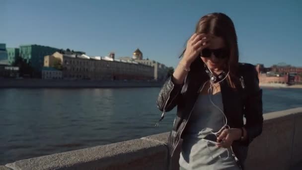 Hermosa chica morena escuchando música en el río con el teléfono — Vídeos de Stock