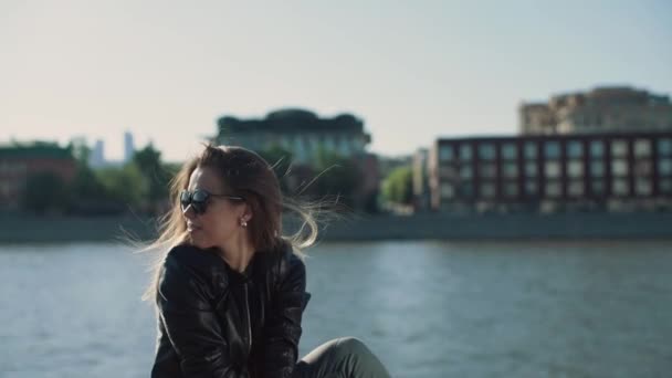 Girl in the wind sits on the waterfront in slowmotion — Stock Video