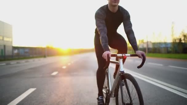 Hombre montando bicicleta de engranajes fijos en la carretera al atardecer — Vídeos de Stock