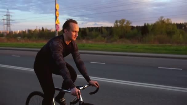 Adam sürme sabit vites bisiklet gün batımında yolda — Stok video