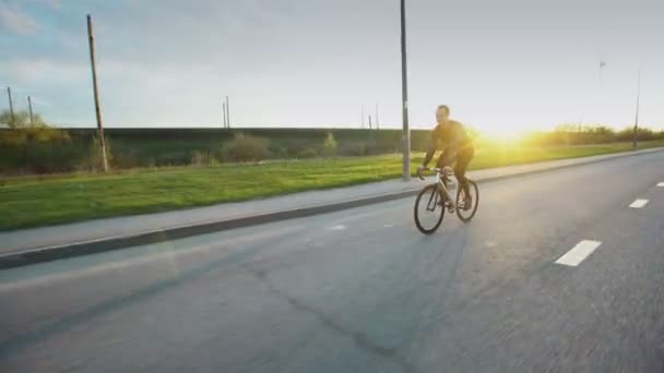 Homem andar de bicicleta de engrenagem fixa na estrada ao pôr do sol — Vídeo de Stock