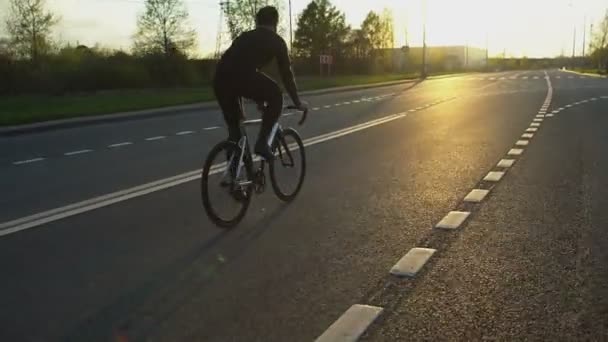 Hombre montando bicicleta de engranajes fijos en la carretera al atardecer — Vídeos de Stock