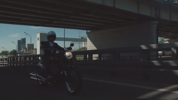 Hombre montando una motocicleta bajo el puente en una ciudad — Vídeo de stock