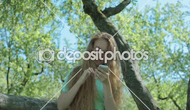 Kızıl saçlı kız seyir telefon elma bahçesi içinde