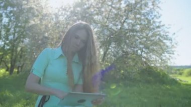 Tablet elma bahçesinde uzun kızıl saçlı kız bakar