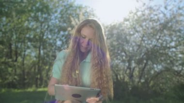 Tablet elma bahçesinde uzun kızıl saçlı kız bakar