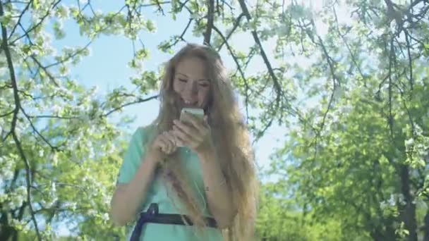 Jeune fille rousse dans le verger de pommes regardant le téléphone — Video