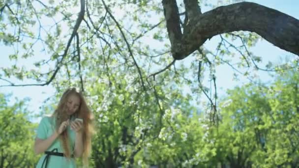 Jonge roodharige meisje in de appelboomgaard kijken naar de telefoon — Stockvideo