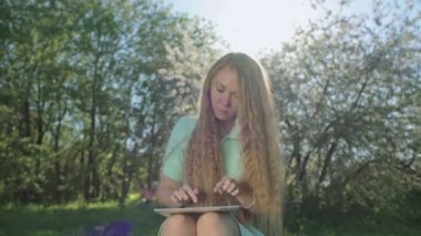 Tablet elma bahçesinde uzun kızıl saçlı kız bakar