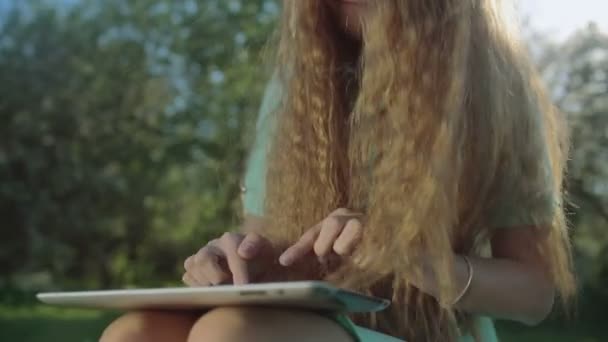 Girl with long red hair looks at tablet in apple garden — Stock Video