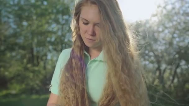 Девушка с длинными рыжими волосами смотрит на табличку в яблоневом саду — стоковое видео