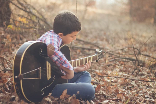 Teenage boy playing guitar in a sunny autumn day — Stock Photo, Image