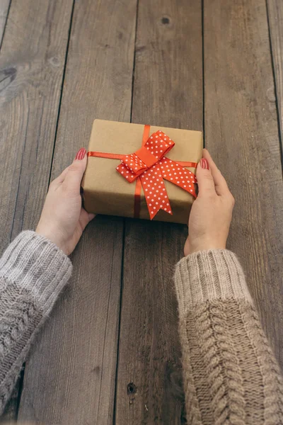 Manos femeninas sosteniendo regalo en mesa de madera —  Fotos de Stock