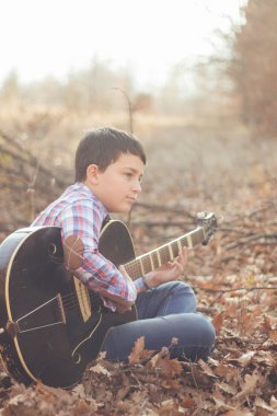 Güneşli bir sonbahar günü gitar ile genç çocuk