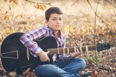 Güneşli bir sonbahar günü gitar ile genç çocuk
