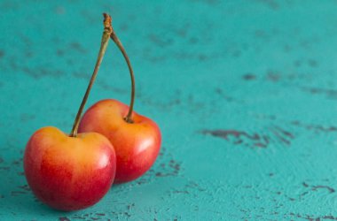 İki Sarı ve Kırmızı Kiraz Bir Teal Tablosu Üzerinde Kökler Bağlı