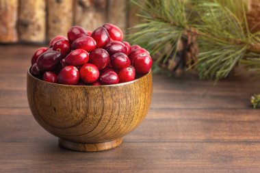 Tahta bir masada taze yuvarlak kırmızı kızılcık kasesi.