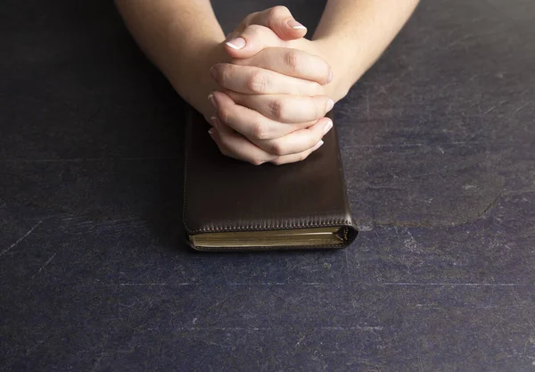 A Woman Praying with Her Hands Clasped on a Bible