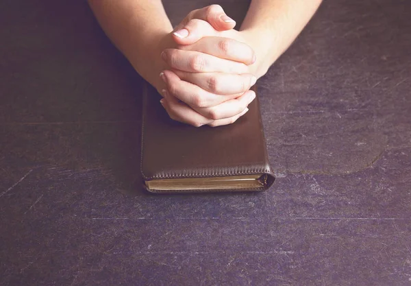 A Woman Praying with Her Hands Clasped on a Bible