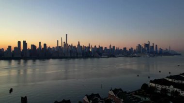 New York City Manhattan gökdelenlerinin güneşli bir günde Hudson nehri boyunca New Jersey, Amerika Birleşik Devletleri 'nden gökyüzü açık 4K hava aracı videosu.