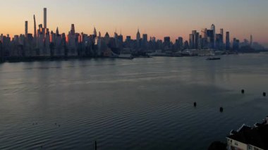 New York City Manhattan gökdelenlerinin güneşli bir günde Hudson nehri boyunca New Jersey, Amerika Birleşik Devletleri 'nden gökyüzü açık 4K hava aracı videosu.