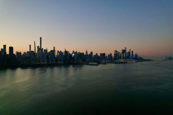 New York City Manhattan gökdelenlerinin güneşli bir günde Hudson nehri boyunca New Jersey, Amerika Birleşik Devletleri 'nden gökyüzü açık 4K hava aracı videosu.