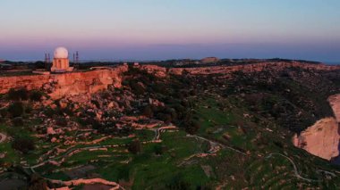 Dingli Kayalıkları 'ndaki Malta' nın en yüksek noktasının insansız hava aracı görüntüsü, gün batımında denize dik bir şekilde düşen yemyeşil çimenler ve kaya oluşumları, altın saat. Güneş altın parıltısını kayalara ve Dingli Radar 'a veriyor.