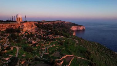 Dingli Kayalıkları 'ndaki Malta' nın en yüksek noktasının insansız hava aracı görüntüsü, gün batımında denize dik bir şekilde düşen yemyeşil çimenler ve kaya oluşumları, altın saat. Güneş altın parıltısını kayalara ve Dingli Radar 'a veriyor.