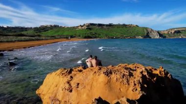 Gozo 'daki en güzel Malta sahilinin hava aracı görüntüsü, berrak mavi suyu ve yemyeşil bitki örtüsüyle büyüleyici dalgaları olan canlı kırmızı Ramla plajı ve güneşli bir günde kont sabahında ünlü Mixta Mağarası arka planı.