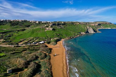 Gozo 'daki en güzel Malta plajının hava aracı görüntüsü, berrak mavi suyuyla canlı kırmızı Ramla plajı ve yemyeşil ile büyüleyici dalgalar ve güneşli bir günde kontun arka planında bulunan ünlü Mixta Mağarası.