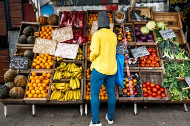 Stock photo of unrecognized woman wearing face mask buying fruit in greengrocer's shop. clipart