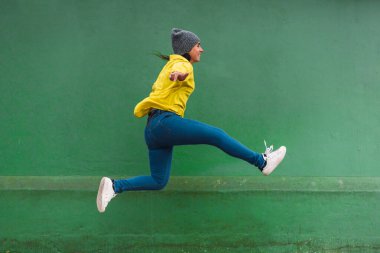 Sarı ceketli mutlu bir kızın sokakta zıplayıp eğlendiğini gösteren bir fotoğraf..