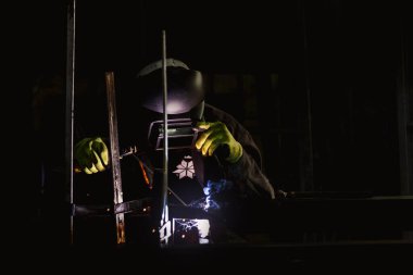 Atölyesinde kaynak lambası kullanarak koruyucu eldiven ve kask takan isimsiz bir işçinin resmi..