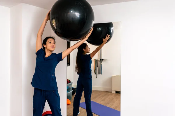 Fizyoterapi kliniğinde elinde pilates topu tutan bir kadın..
