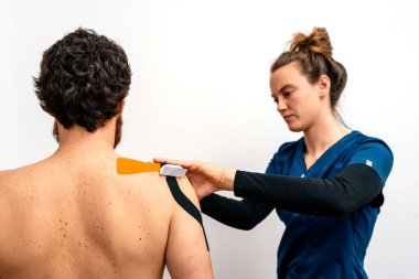 Sedyede oturan hastaya bant tedavisi uygulayan fizyoterapistin resmi..