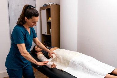 Fizyoterapi kliniğinde kadın işçi hastaların ellerini bandajla sarıyor. Kapat..