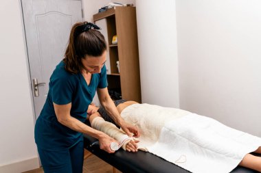 Fizyoterapi kliniğinde kadın işçi hastaların ellerini bandajla sarıyor..