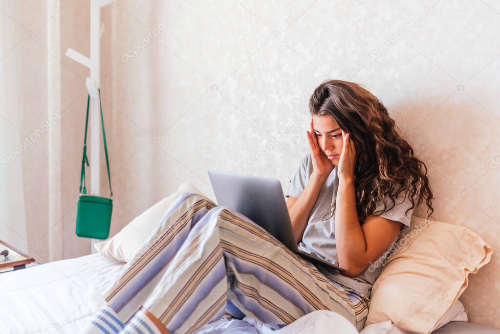 Stock photo of stressed girl in pajamas using computer in the bed.