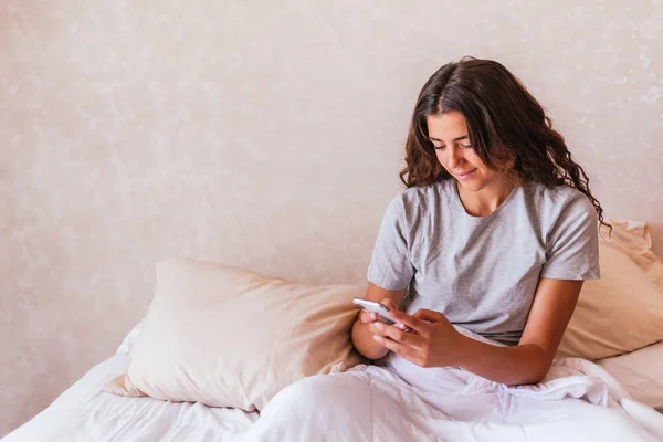 Yatakta cep telefonunu kullanan pijamalı mutlu bir kız resmi..