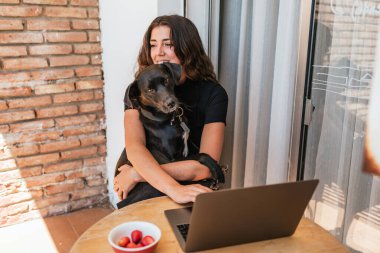 Köpeğiyle birlikte balkonda bilgisayarla video görüşmesi yaparken ve meyve yerken çekilmiş mutlu bir fotoğraf..
