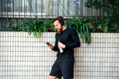 Mutlu sakallı adam dışarıda antreman yaptıktan sonra telefonunu kullanıp müzik dinliyor..