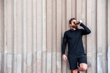 Dışarıda antreman yaptıktan sonra kulaklıklı, su içen mutlu sakallı adam..