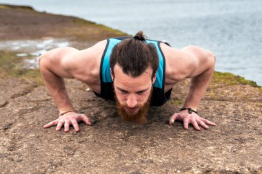 Odaklanmış sakallı adam deniz kenarında şınav çekiyor..