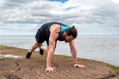 Odaklanmış sakallı adam deniz kenarında şınav çekiyor..